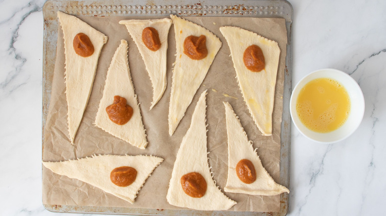 Unrolled crescent rolls with pumpkin filling next to bowl of egg wash