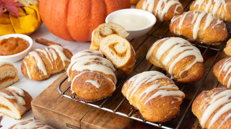 Glazed pumpkin crescent rolls next to pumpkin and bowl of cream cheese glaze