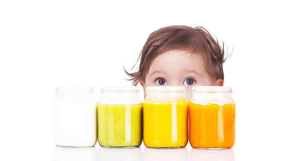 Baby peeking over jars of baby food