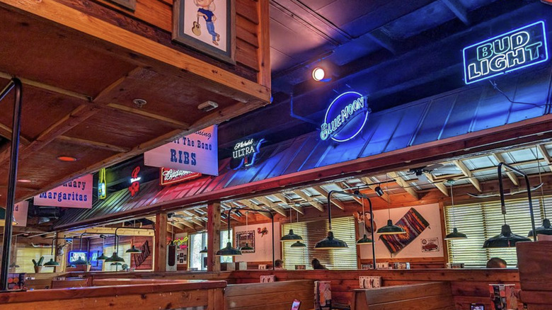 The interior of a Texas Roadhouse restaurant with booths, wood paneling, and neon beer signs