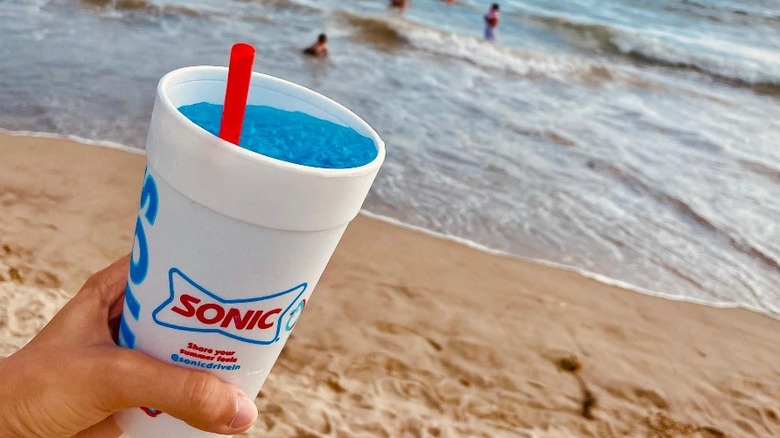 a person holding a sonic drink by the beach