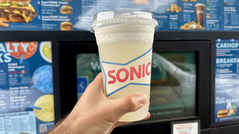 hand holding Sonic lemonade near drive thru menu