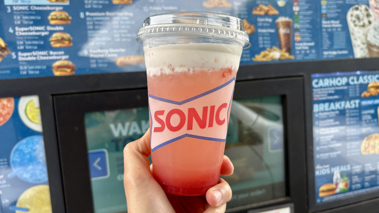 hand holding Sonic lemonade near drive thru menu
