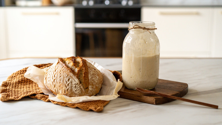 Sourdough bread and a bottle of sourdough starter on a white countertop