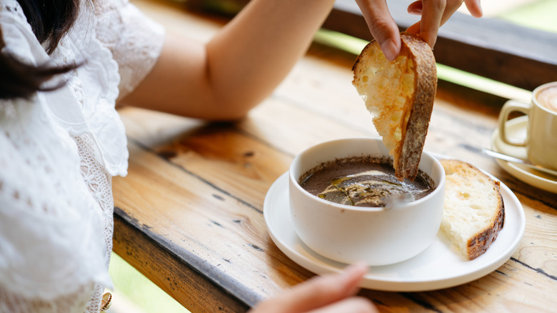 A woman dipping a slice of sourdough on a bowl of soup