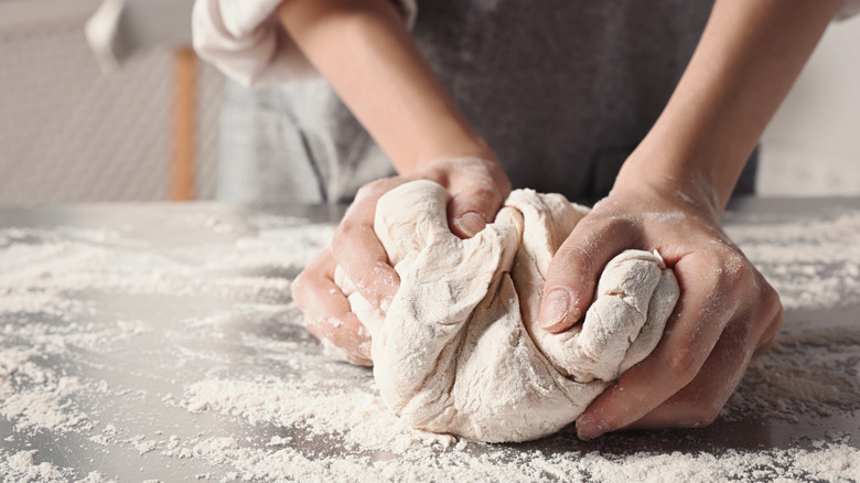 Two hands kneading dough on a table dusted with flour