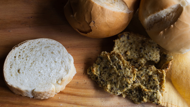 A slice of whole wheat bread next to crumbled whole grain bread and other artisanal loaves