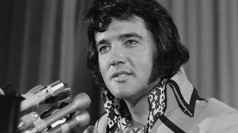 Elvis Presley at a public event in front of multiple microphones.
