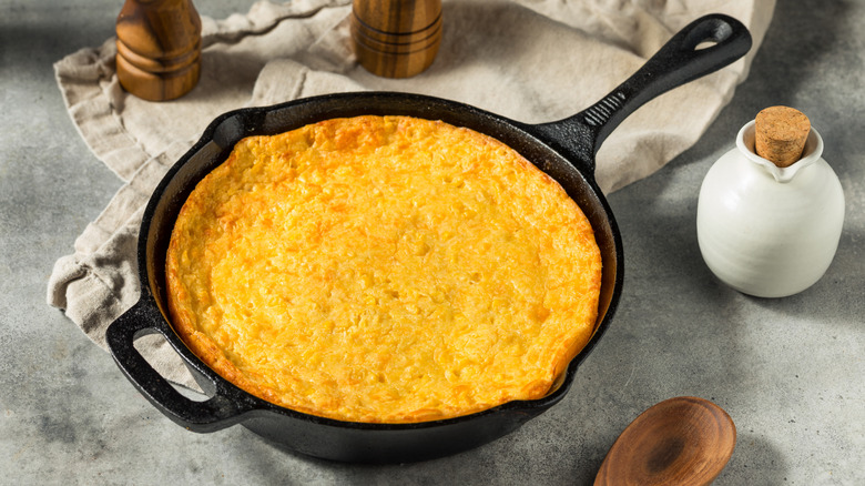 Spoon cake or cornbread casserole pudding in cast iron pan on table