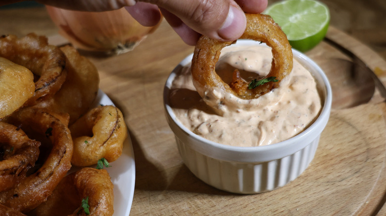 hand dipping beer battered onion ring into ramekin of creamy Southwestern dipping sauce