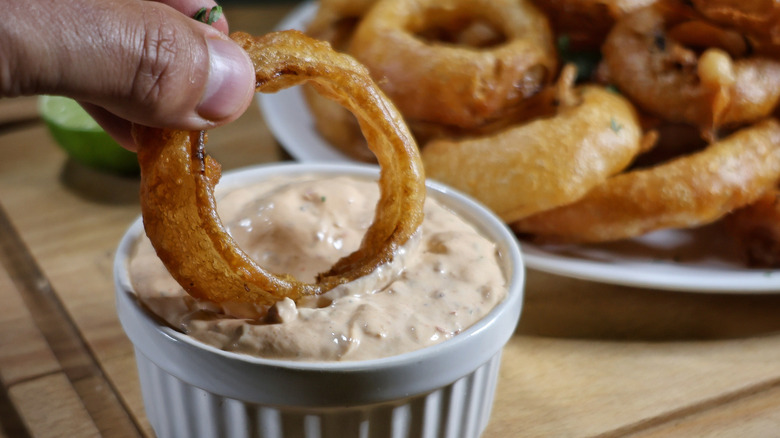 hand dipping beer battered onion ring in ramekin of creamy sauce