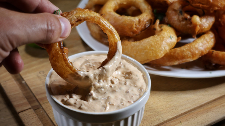 hand dipping Southwestern-style beer battered onion ring into ramekin of creamy dipping sauce