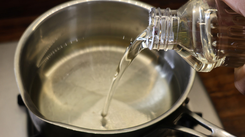 vegetable oil pouring from bottle into metal pot