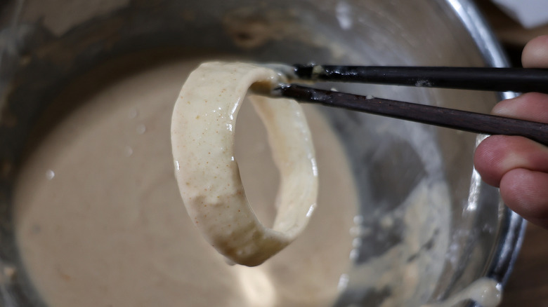 chopsticks holding onion ring coated in batter above mixing bowl of batter