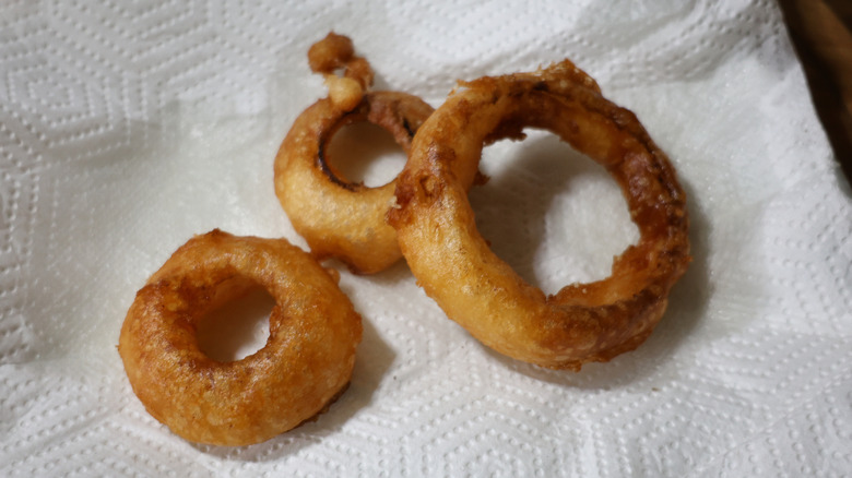 three fried beer battered onion rings on plate lined with paper towels
