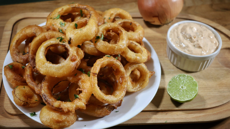 plate of beer battered onion rings on cutting board with ramekin of dipping sauce and sliced lime