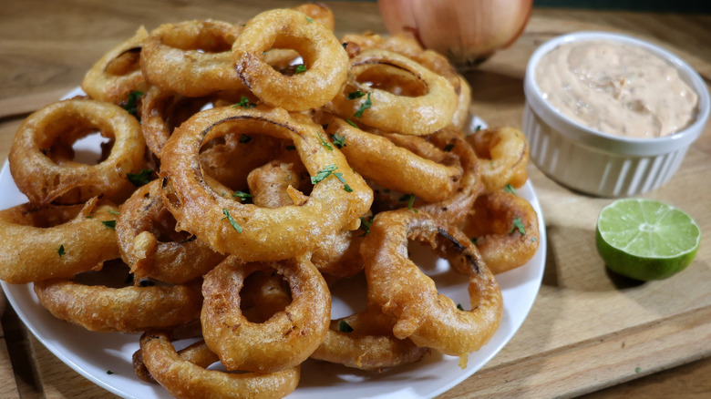 plate of Southwestern-style beer battered onion rings on cutting board next to ramekin of sauce and sliced lime