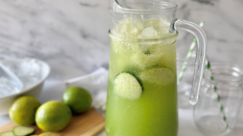 Sparkling cucumber limeade in pitcher with limes and glasses in background