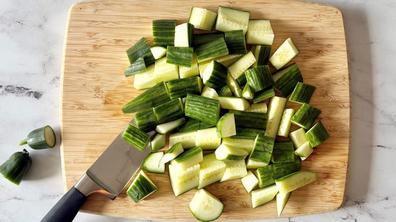 Chopped cucumbers and knife on wooden board