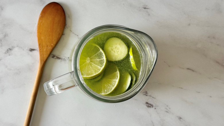 Pitcher full of limeade, lime slices, and cucumber slices next to wooden spoon