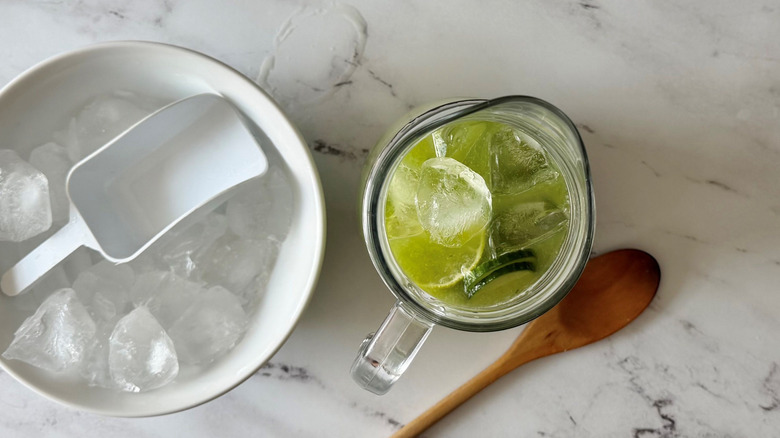 Bowl of ice next to limeade in pitcher and wooden spoon