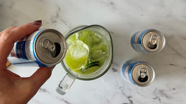 Hand pouring can of club soda into pitcher with limeade