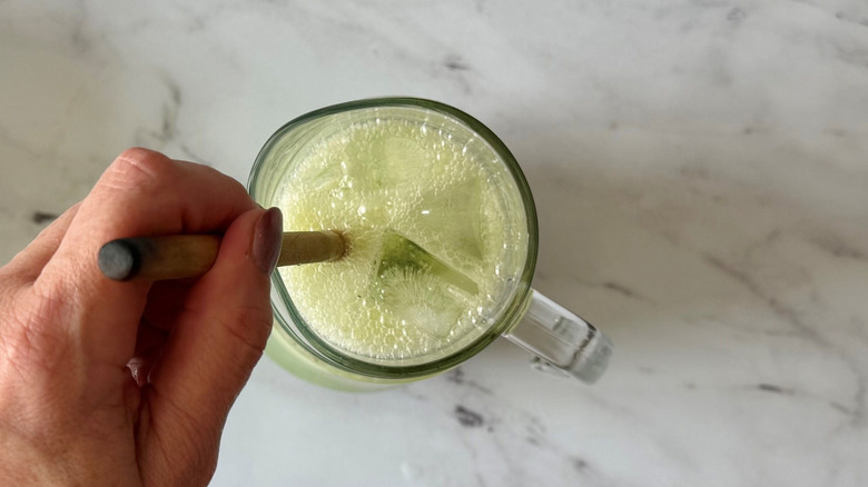 Hand using wooden spoon to stir limeade in pitcher