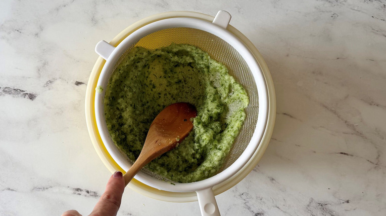 Wooden spoon pressing cucumber puree through sieve