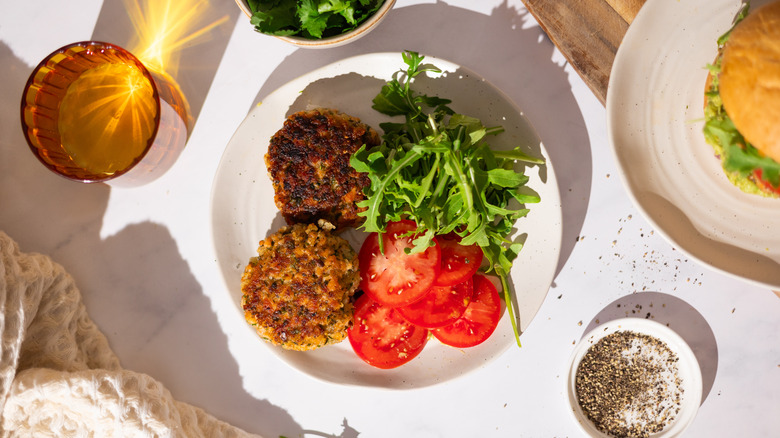 salmon burger patties on plate with tomatoes and arugula salad