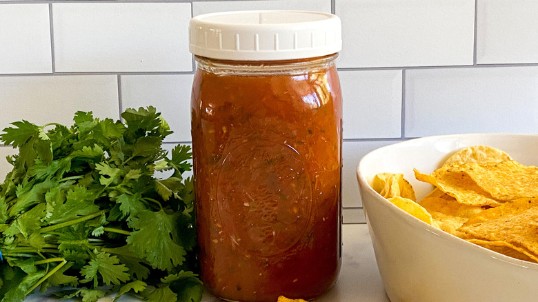 Spicy Salsa Roja Recipe in a mason jar with tortilla chips in bowl and fresh cilantro sprigs