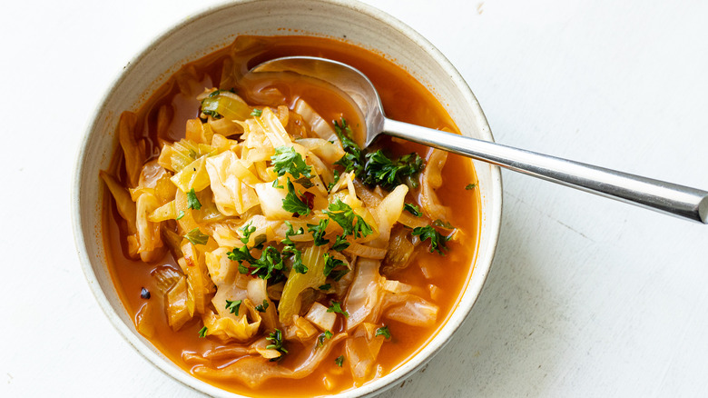 Spicy cabbage soup in white bowl with metal spoon