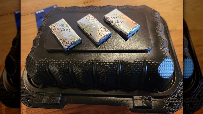 An Olive Garden takeout box with three chocolate mints on top.