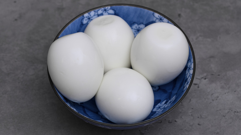 Four hard-boiled eggs in a blue and white bowl on a gray background
