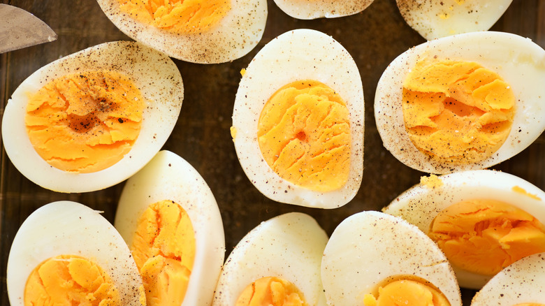 A close-up of hard-boiled eggs cut in half, sprinkled with salt and pepper, on a black countertop.