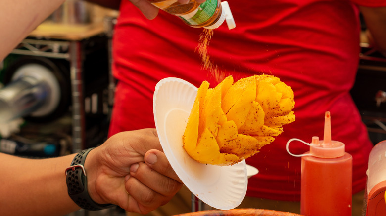 Street vendor sprinkling Tajín over mango flower.