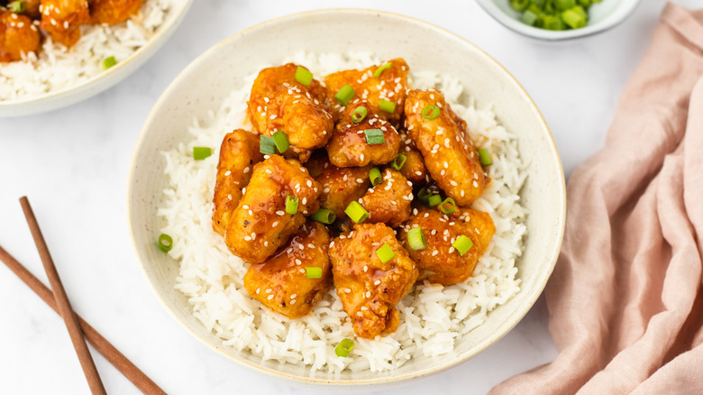 Bowl of crispy glazed chicken with rice and chopped green onions