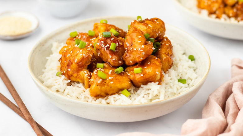 Bowl of crispy glazed chicken with rice and chopped green onions