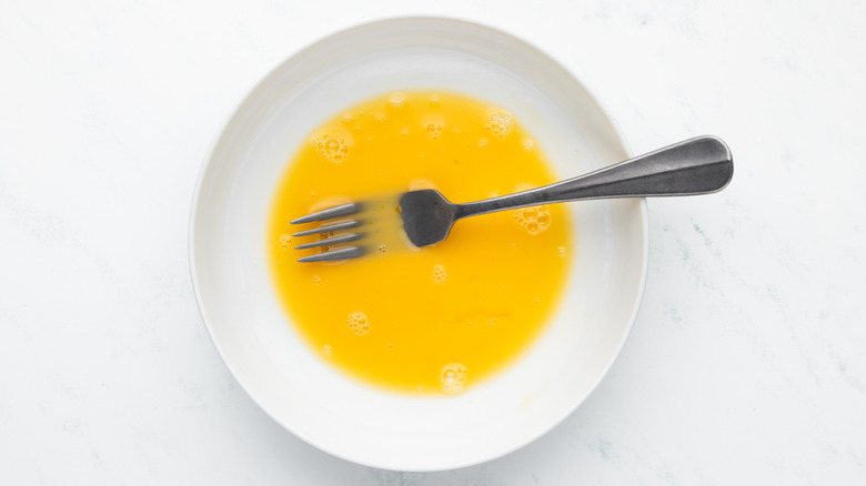 Beaten egg in white dish with fork