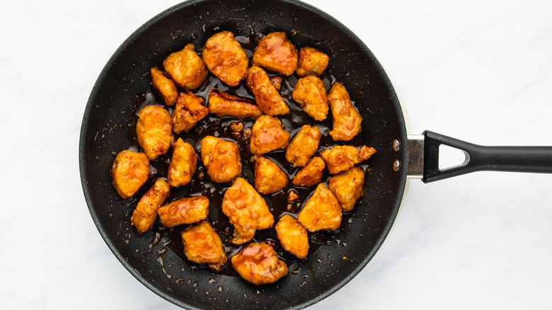 Sauce-coated crispy chicken pieces in frying pan