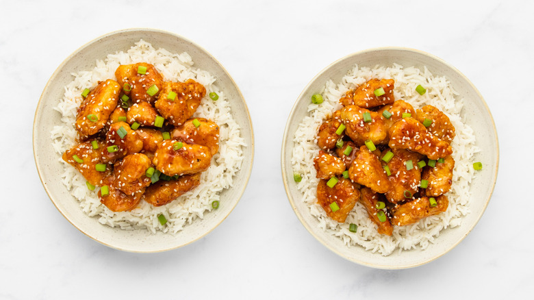 Two bowls of crispy glazed chicken with rice and chopped green onions