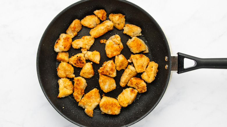 Crispy chicken pieces cooking in frying pan