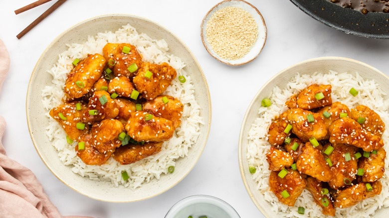 Two bowls of crispy glazed chicken with rice and chopped green onions