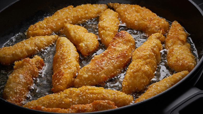 Chicken tenders or chicken strips frying in a pan in shallow oil.