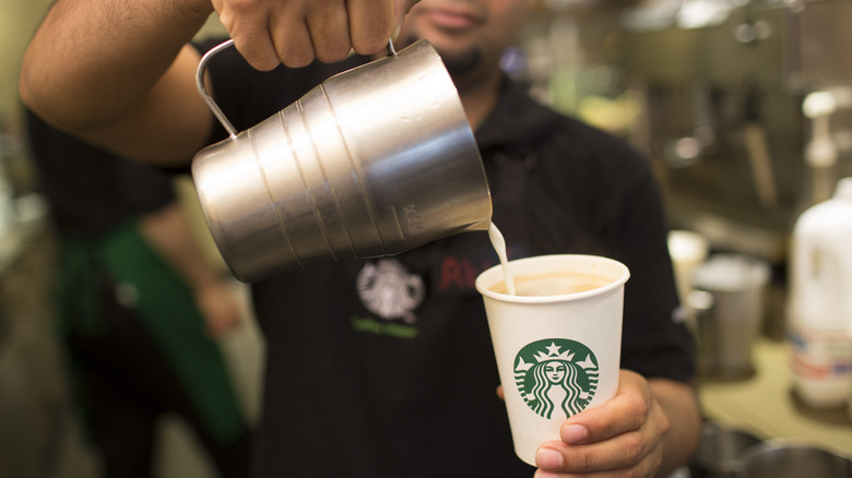 A Starbucks employee pouring milk into a cup