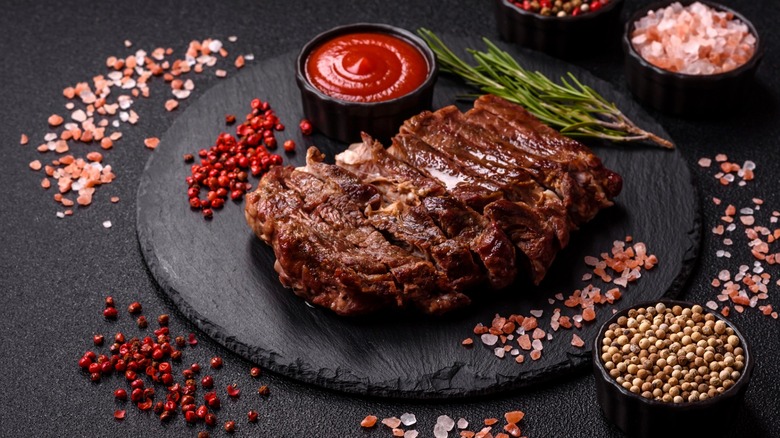 Sliced seared steak served with multiple seasonings and ketchup.