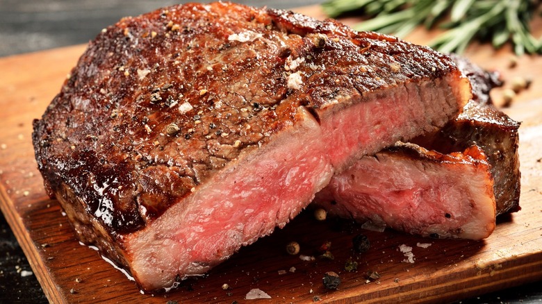 Grilled steak with coarse salt and seasonings on a wooden cutting board