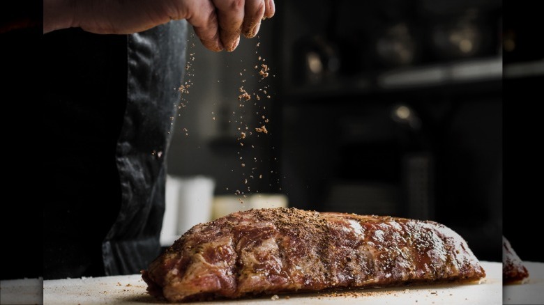 Hand seasoning a cooked steak on a cutting board