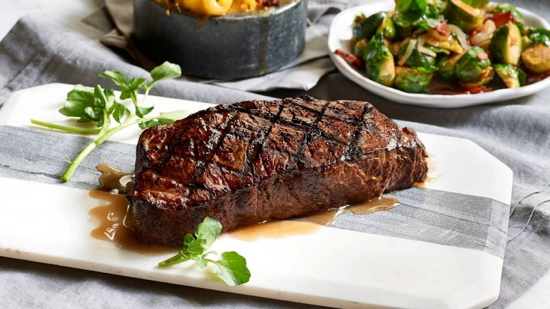 Morton's Steakhouse ribeye on wooden board, with mac & cheese and Brussels sprouts in background
