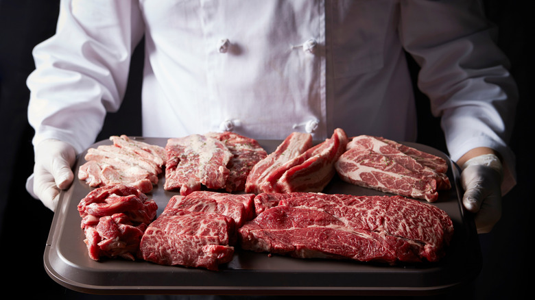 Various cuts of beef held on a tray by a chef