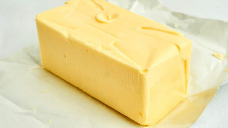 A whole stick of butter peeled away from it's wrapper, sitting on a countertop.